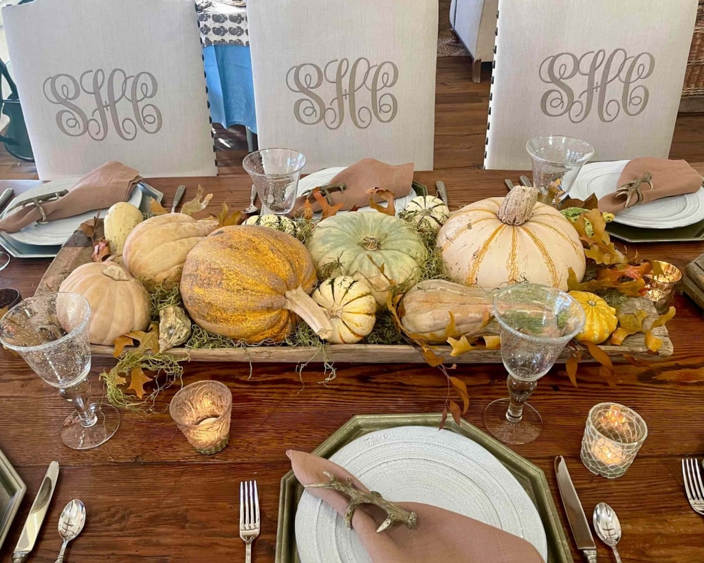 thanksgiving table with bowl of pumpkins and monogrammed chairs